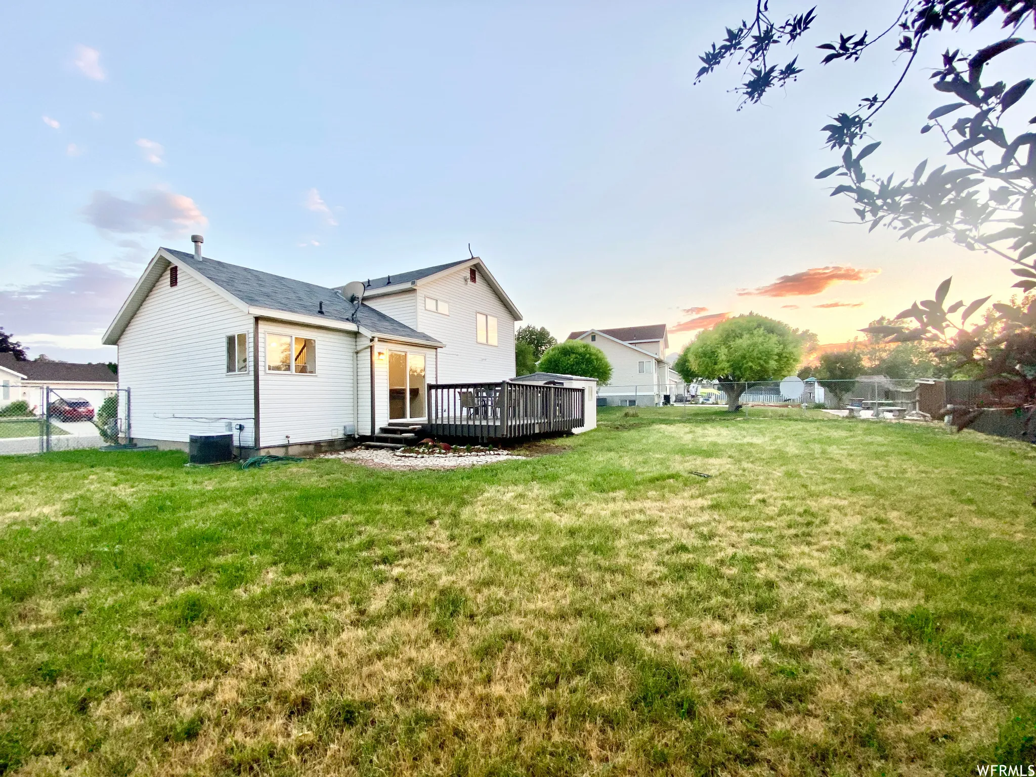 Expansive backyard with a wooden deck, sliding glass door access, white vinyl siding, and a chain-link fence