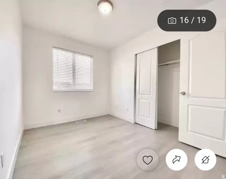 Interior room featuring light wood-finish flooring, white walls, and a window with horizontal blinds