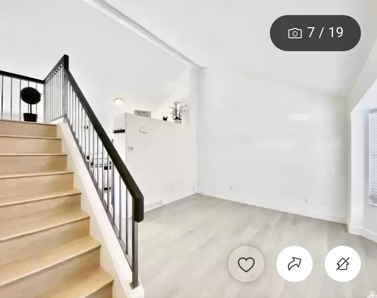 Interior space featuring light wood-finish flooring, a contemporary staircase with metal balusters and dark handrail, vaulted ceilings, and a bay window with horizontal blinds