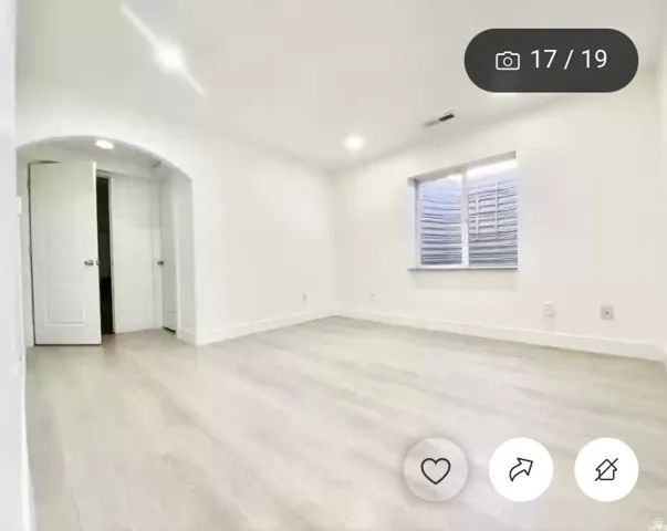 Spacious room featuring light wood-finish flooring, white walls, and a window with blinds