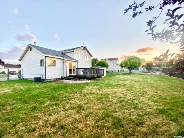 Expansive backyard with a wooden deck, sliding glass door access, white vinyl siding, and a chain-link fence