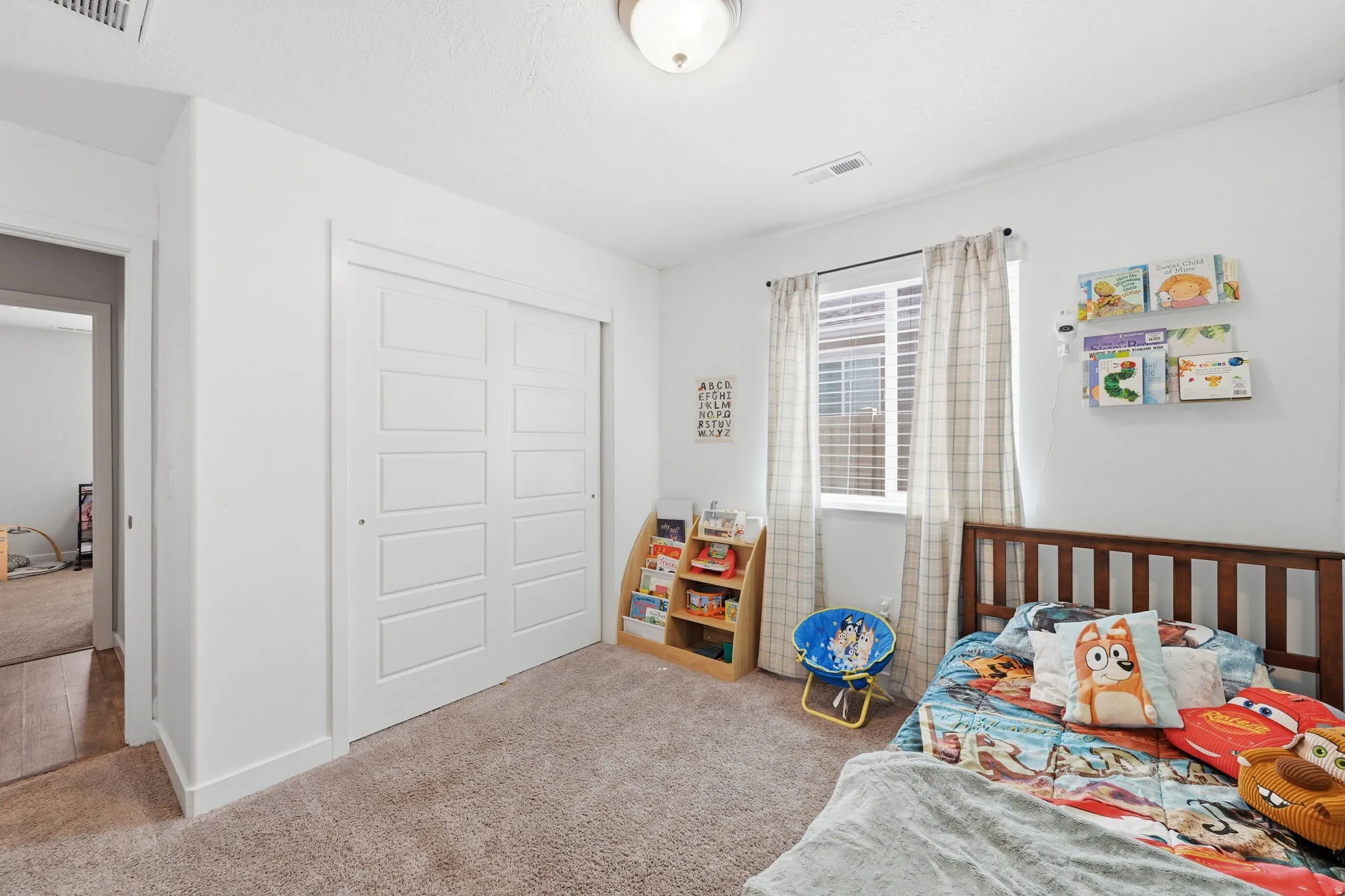 Bright room featuring a window with blinds, a ceiling-mounted light fixture, and plush carpeting