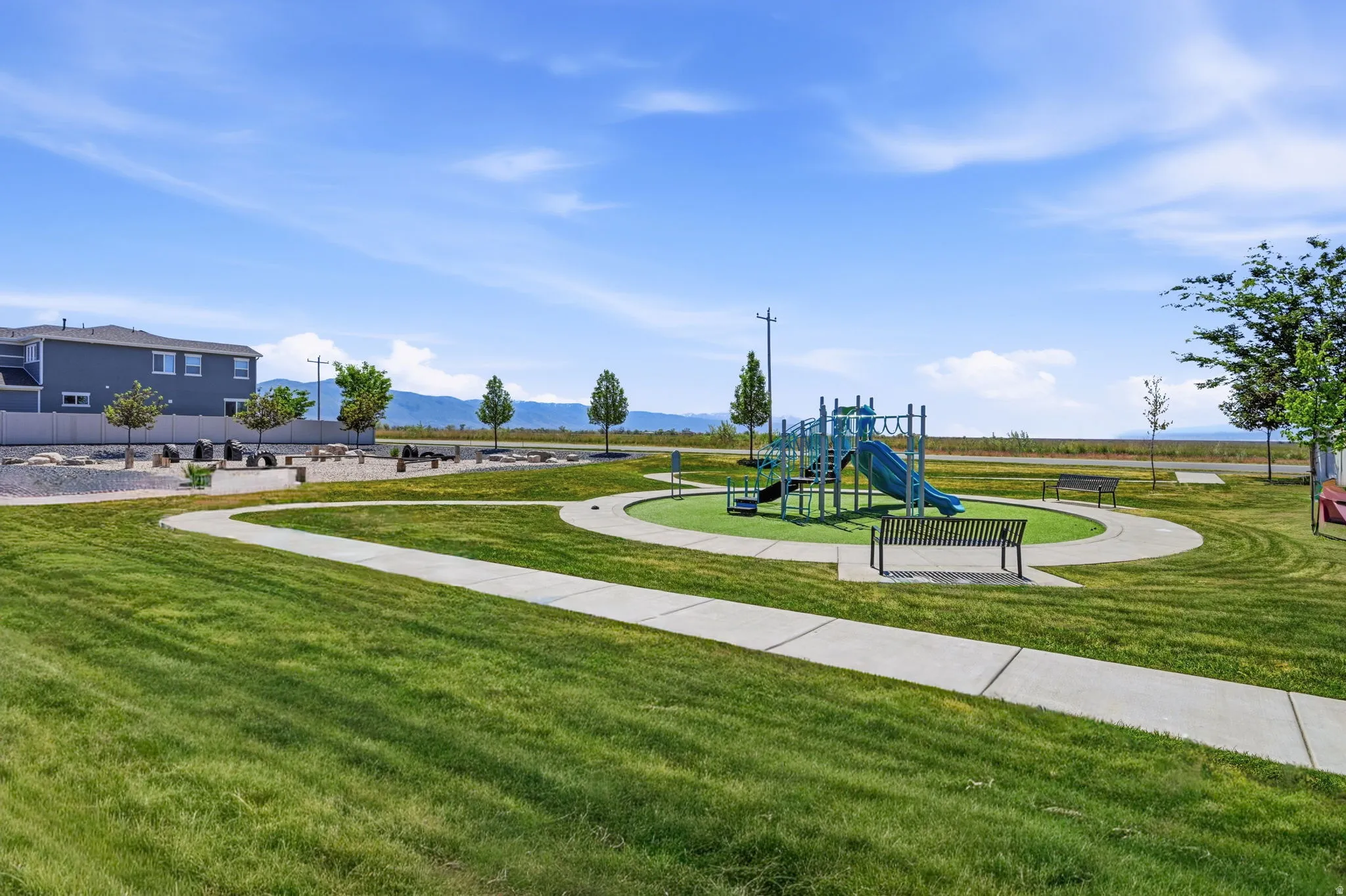 Community playground area featuring a blue and green play structure, a surrounding artificial turf surface, and multiple benches
