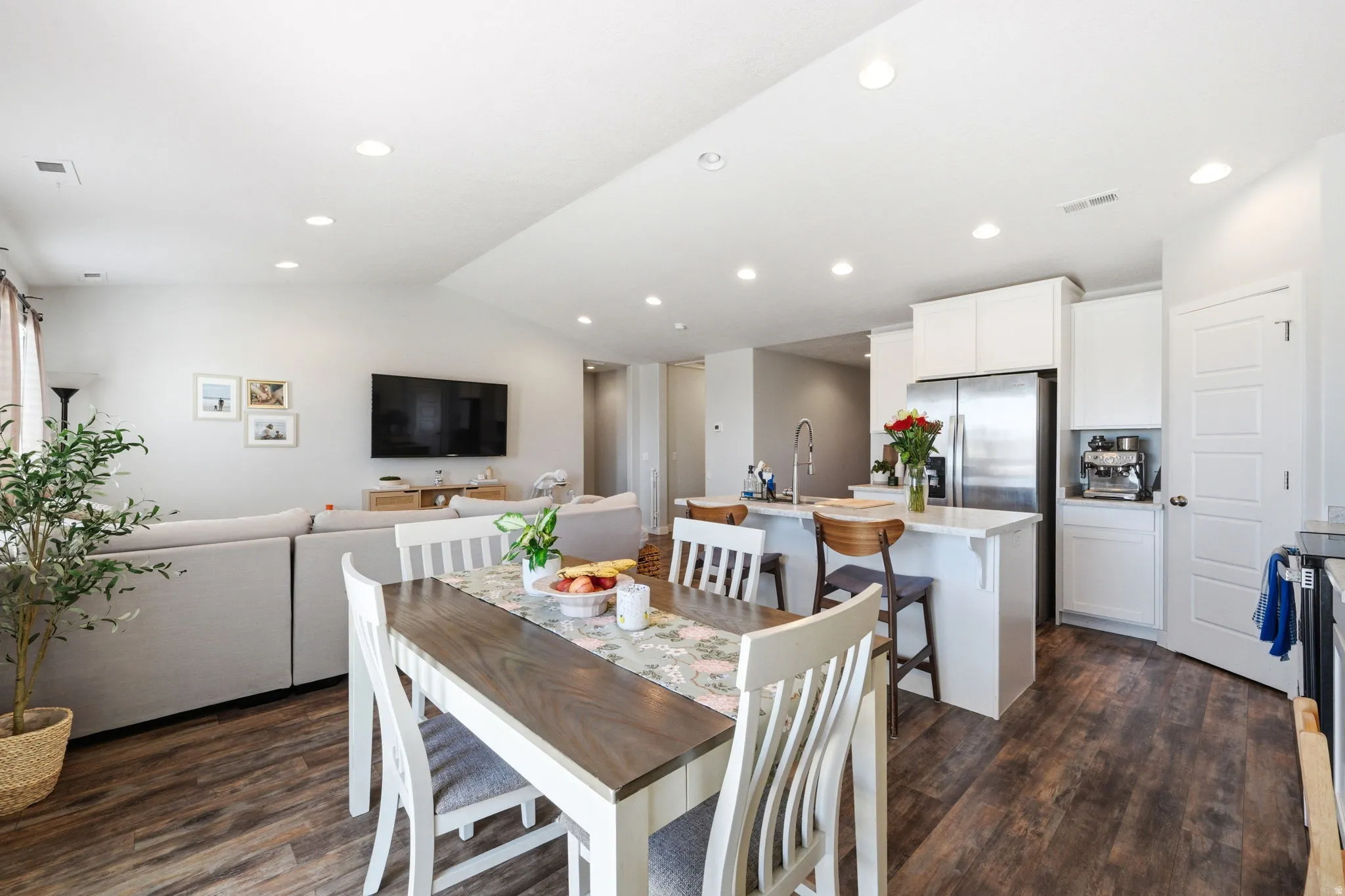 Open-concept living space featuring wood-finish flooring, recessed lighting, and a white kitchen with stainless steel appliances