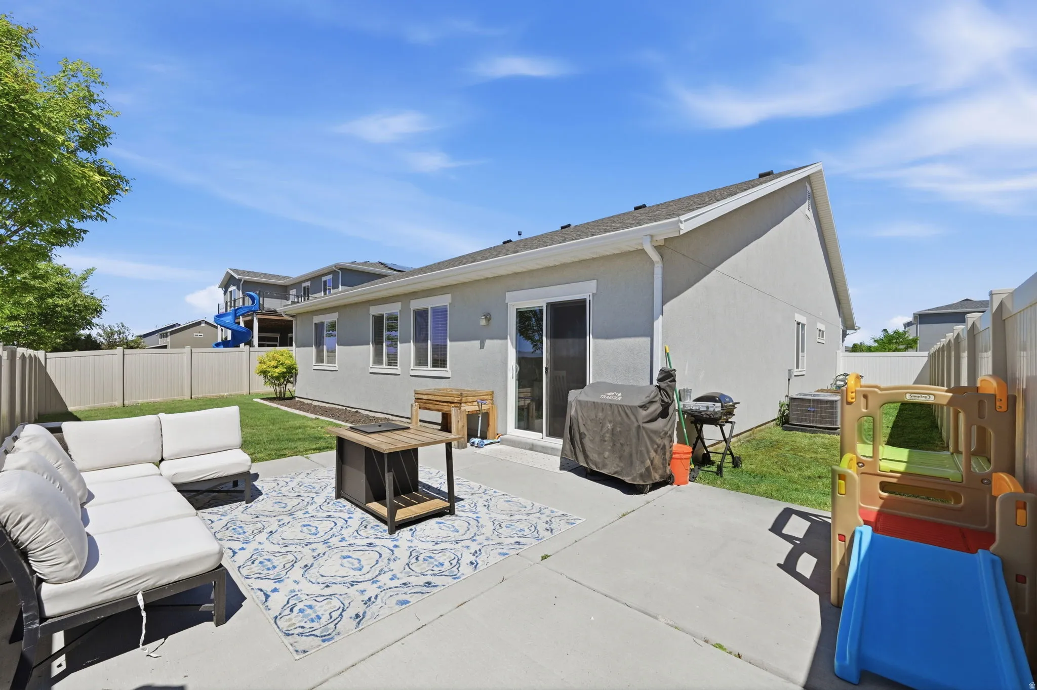 Rear exterior featuring a concrete patio, sliding glass door, multiple windows, and a fenced backyard with a grass lawn