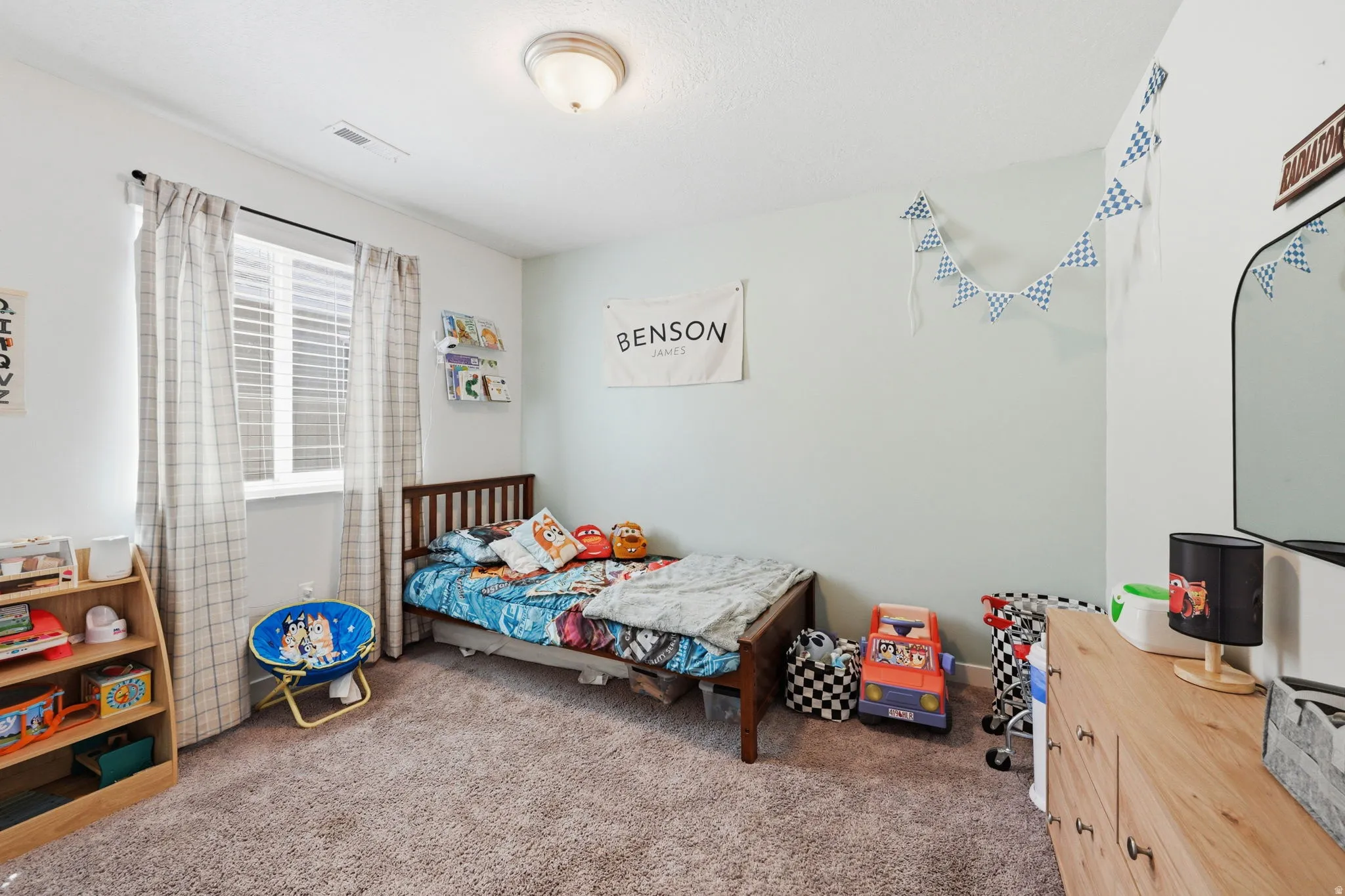 Carpeted bedroom featuring a window with blinds and curtains, light blue wall accent, and a flush mount ceiling light fixture