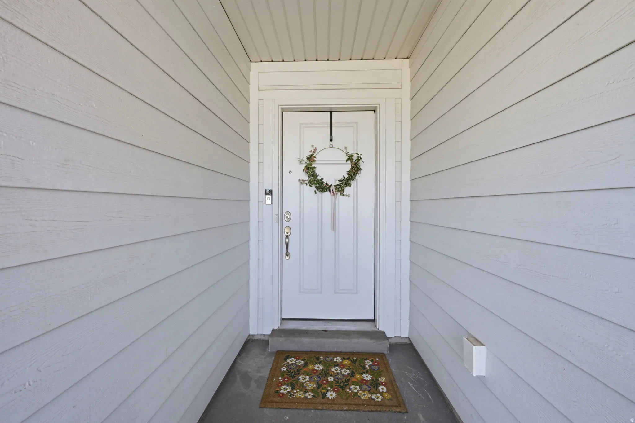 Entryway featuring white panel siding, a white front door with a full-view storm door, and a covered porch with a concrete slab