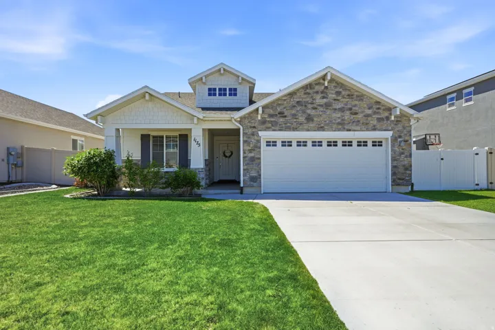 Stone facade and shake siding exterior featuring a covered entry, an attached two-car garage, an extended concrete driveway, and a manicured lawn