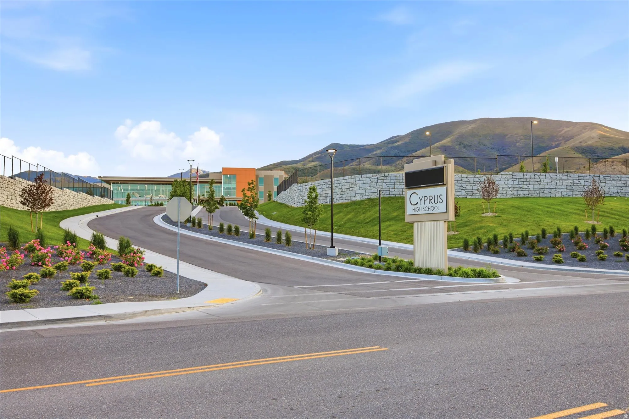 Modern educational facility featuring contemporary architecture, extensive glass facades, a prominent signage display, a paved entryway, and landscaped grounds with mature trees and flowering shrubs