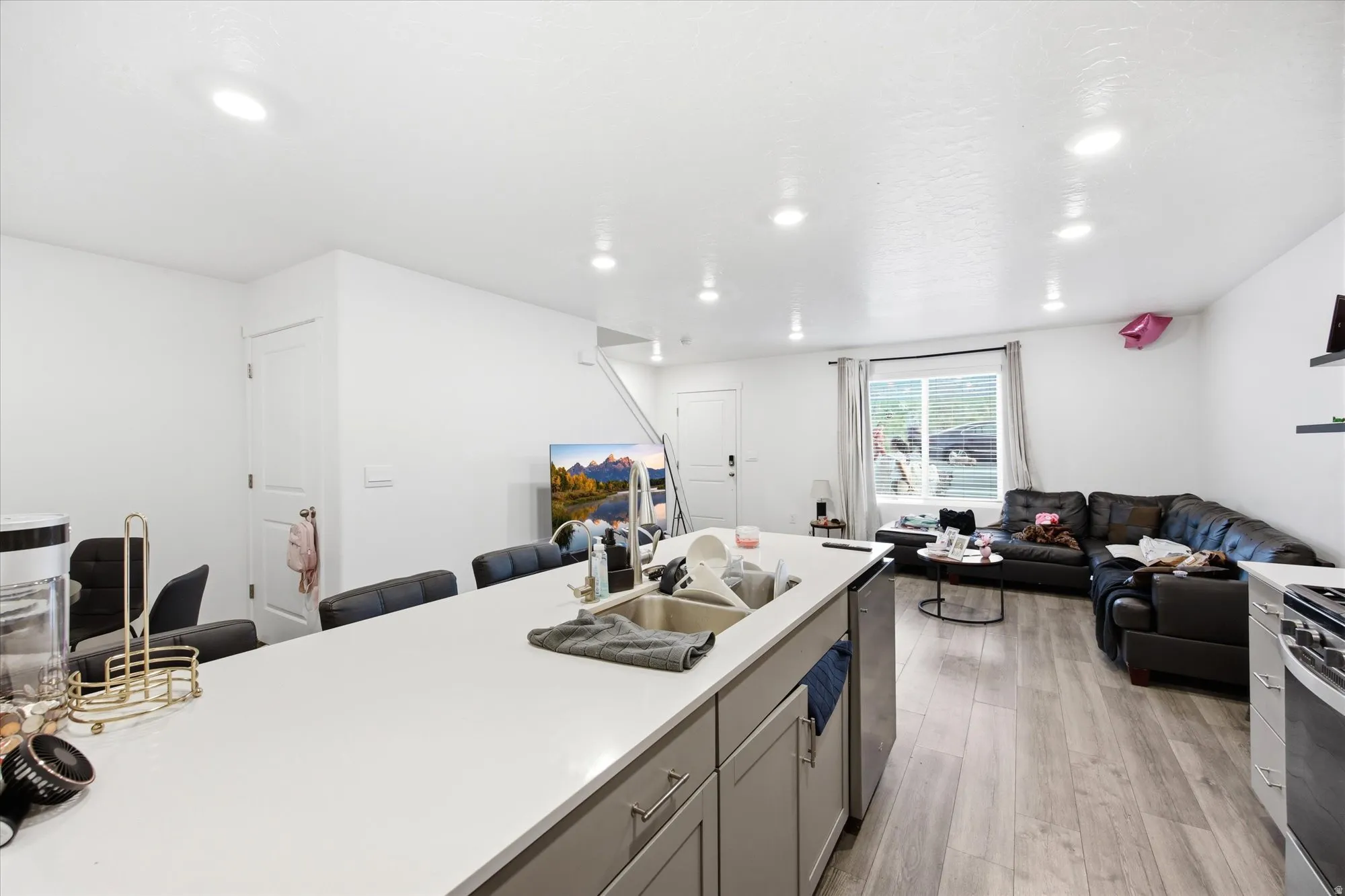 Open-concept living area featuring a kitchen island with a built-in sink, light wood-finish flooring, recessed lighting, and a white color palette