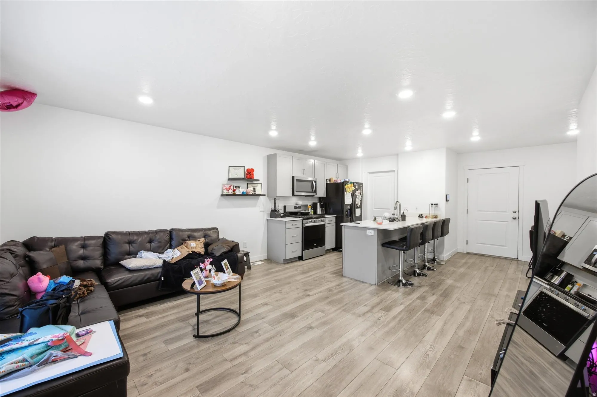 Open-concept living space featuring wood-finish flooring, recessed lighting, white walls, a kitchen island with seating, and gray cabinetry