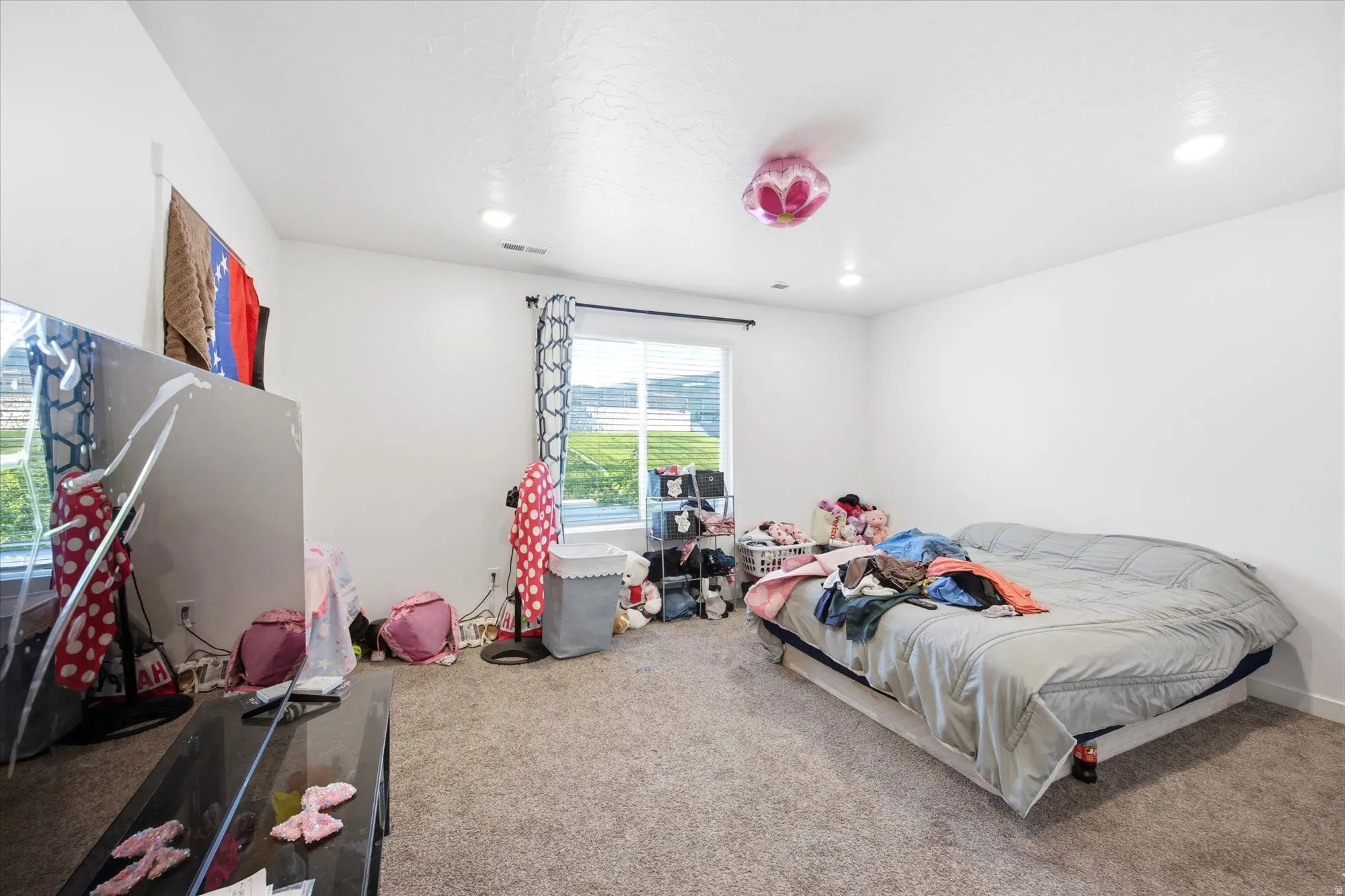 Carpeted room featuring a large window with blinds and patterned curtains