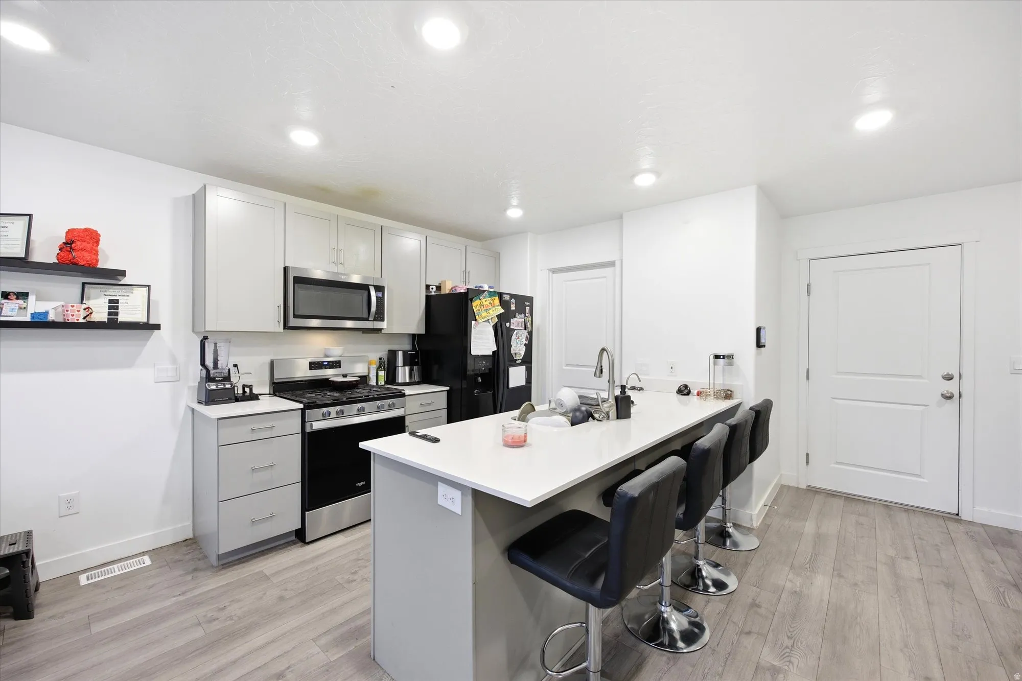 Modern kitchen featuring light gray cabinetry, stainless steel appliances, and wood-finish flooring
