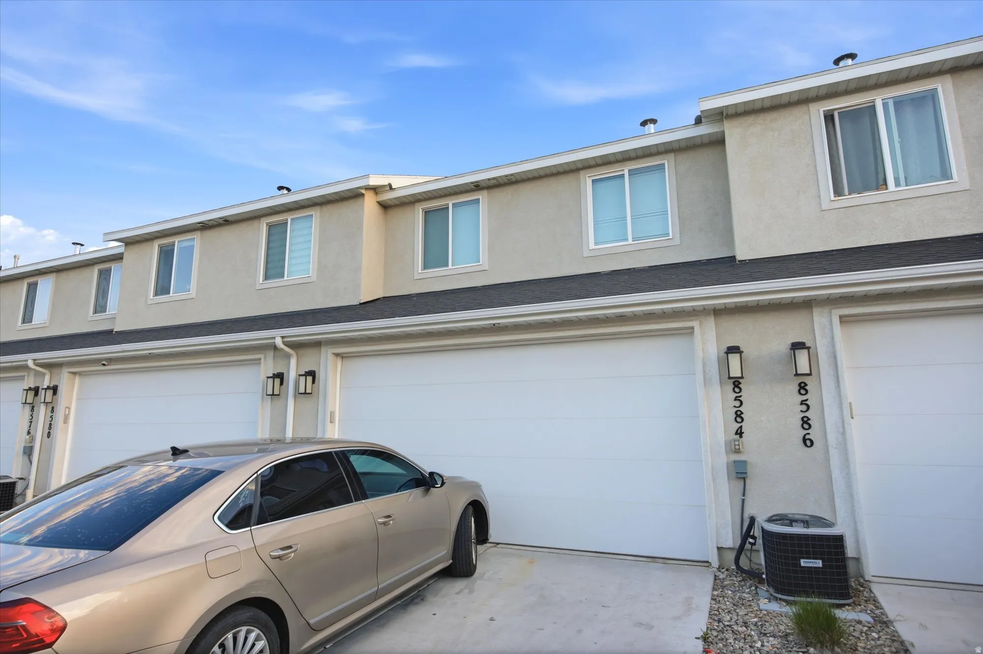 Multi-level exterior featuring light-colored stucco, white-framed windows, and a dark shingle roof