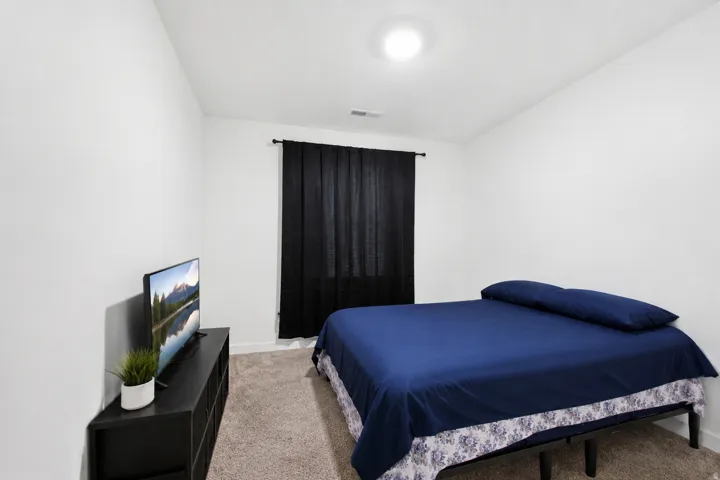 Carpeted room featuring white walls, a ceiling-mounted light fixture, and a window with dark curtains