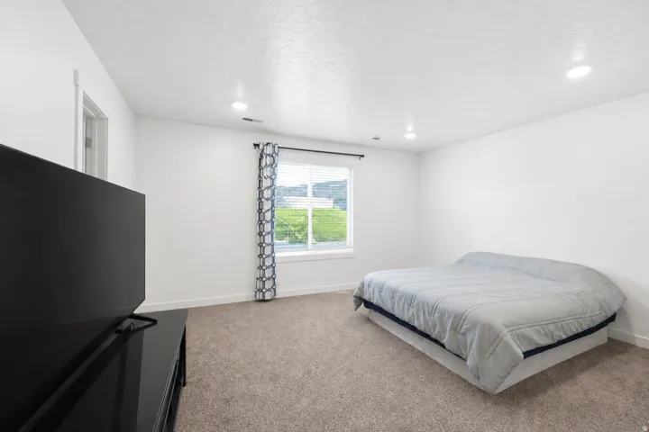 Bright room featuring a window with blinds, recessed lighting, and neutral-toned carpeting