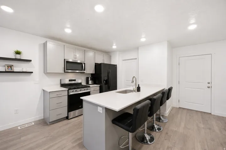 Modern kitchen featuring light gray cabinetry, stainless steel appliances, and a central island with a sink