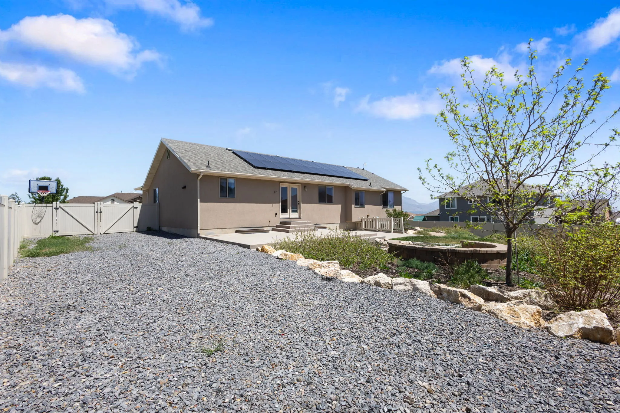 Rear exterior featuring a neutral-toned stucco finish, a composite shingle roof, and integrated solar panels