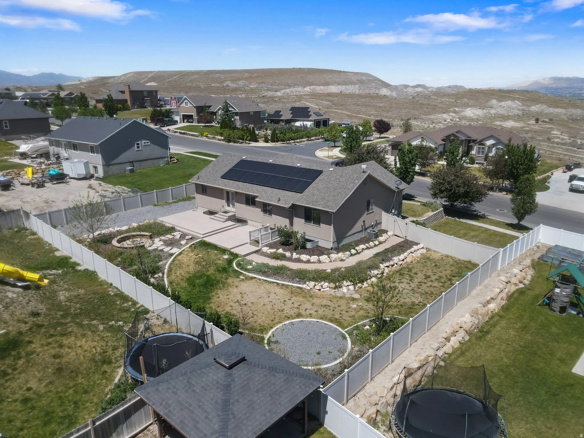 Rear exterior featuring an elevated patio, solar panels, and a fenced yard with a fire pit area