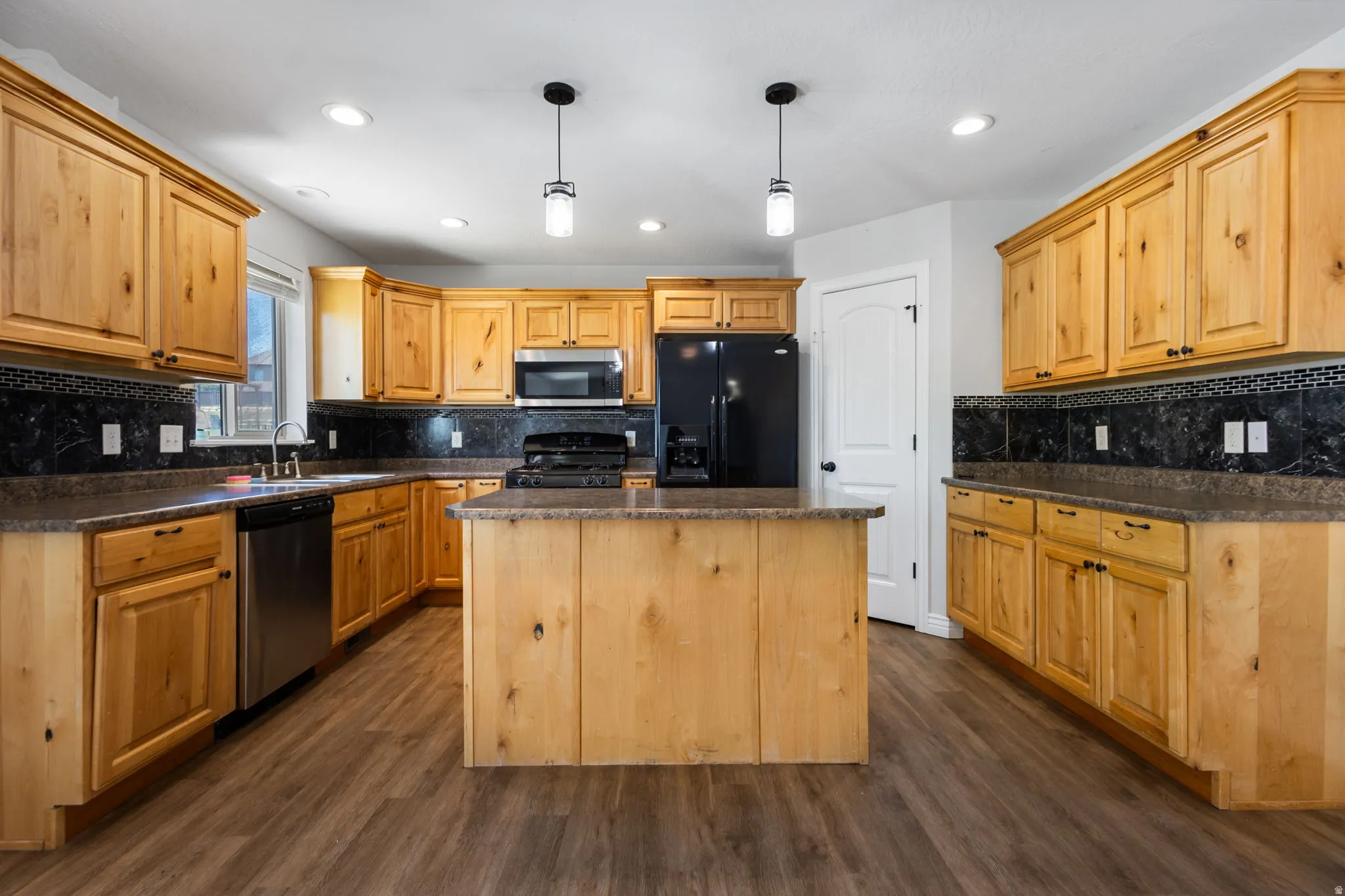 Kitchen featuring light wood cabinetry, a central island, dark countertops, and a mosaic tile backsplash
