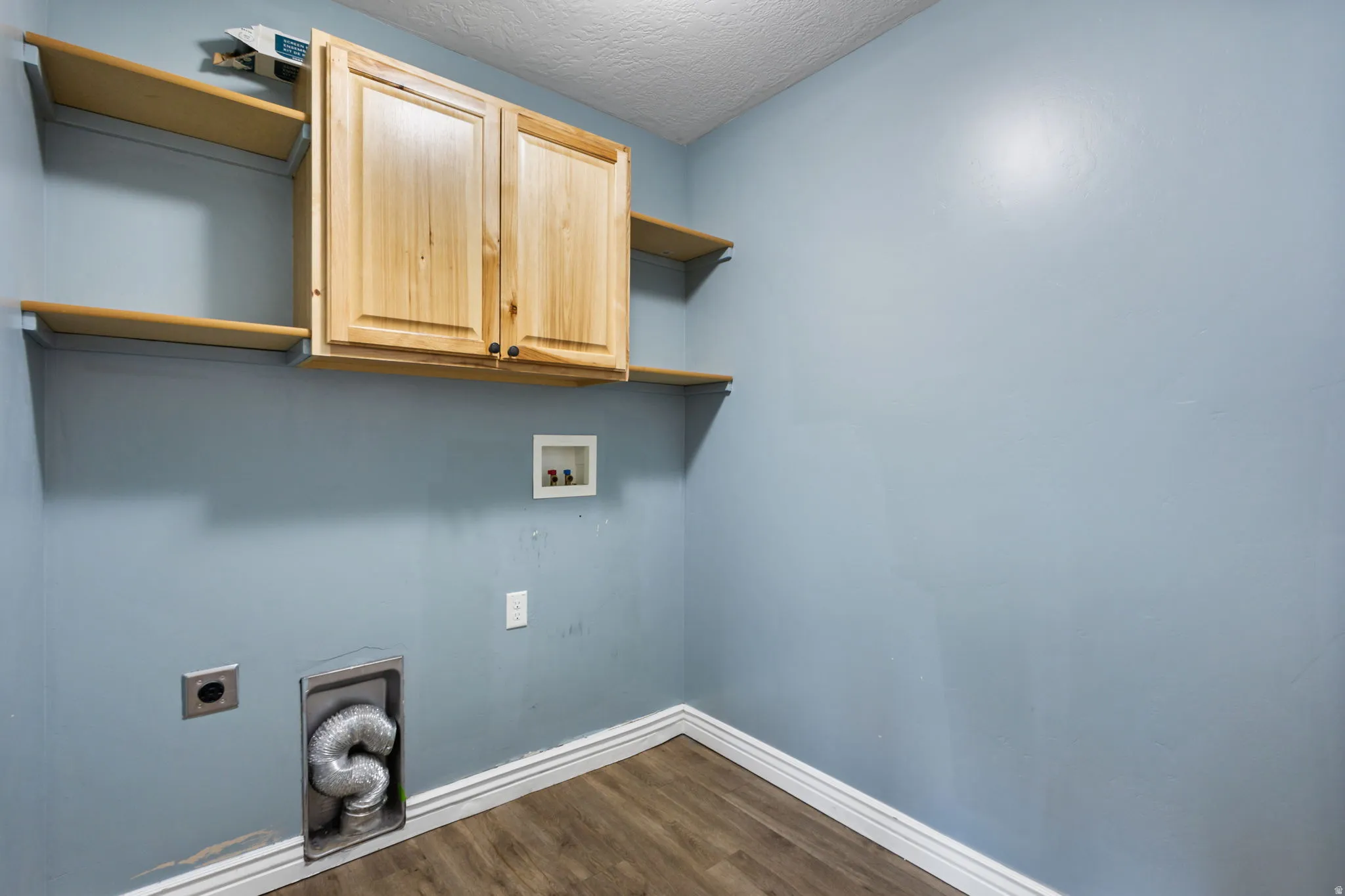 Utility room featuring wood-finish flooring, light blue walls, and white baseboards