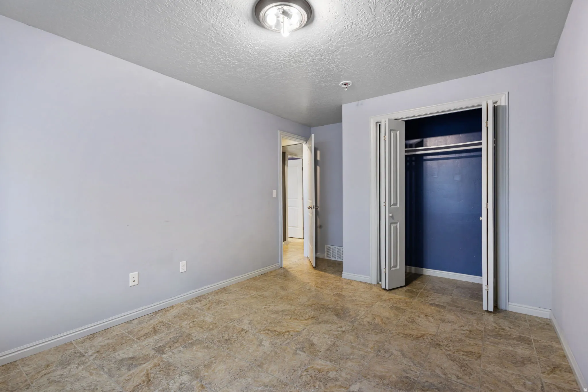 Spacious room featuring neutral wall tones, textured ceiling, a ceiling-mounted light fixture, bi-fold closet doors, and wood-finish flooring
