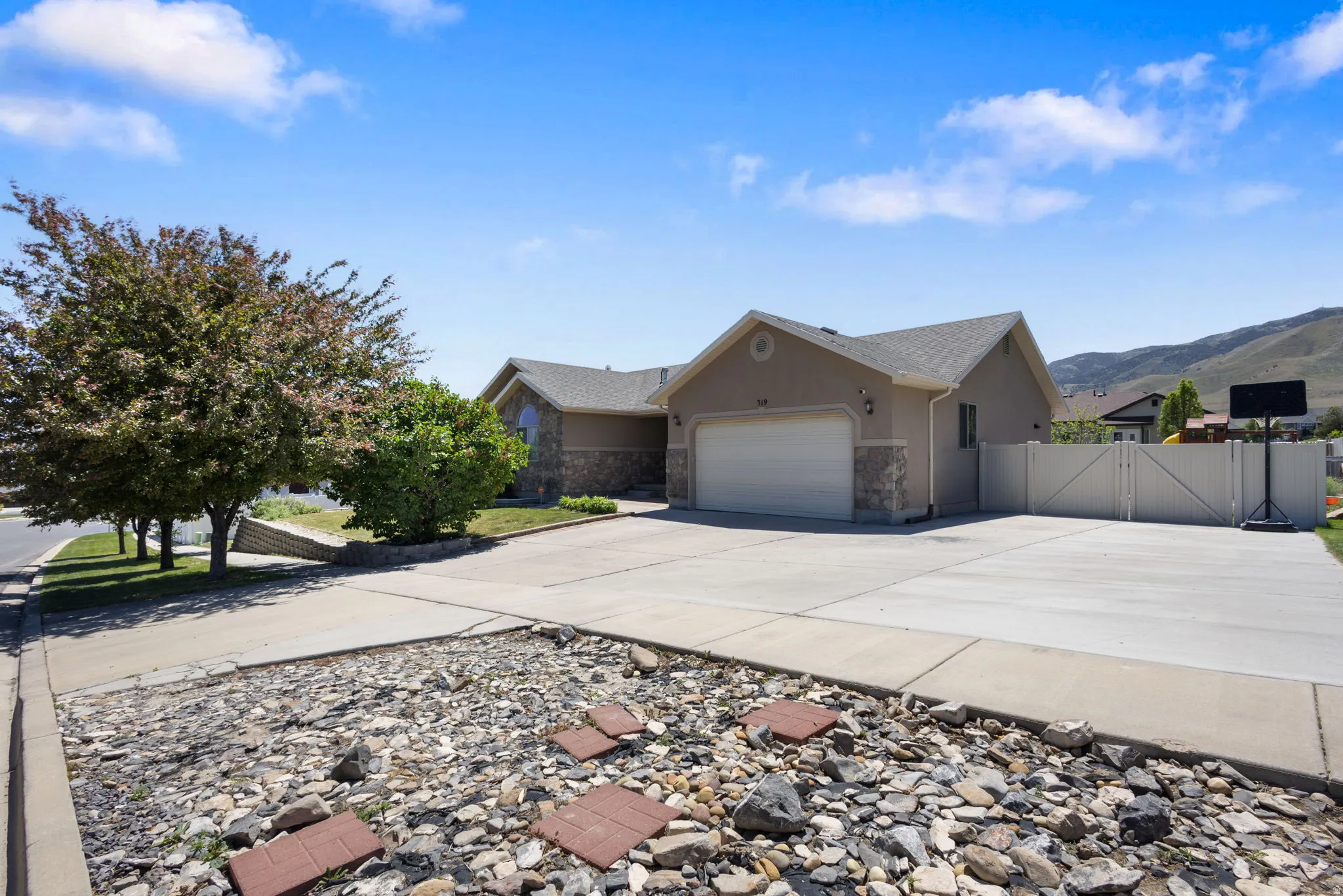 Contemporary stucco and stone-accented residence featuring a two-car garage, expansive concrete driveway, and side yard with a privacy fence