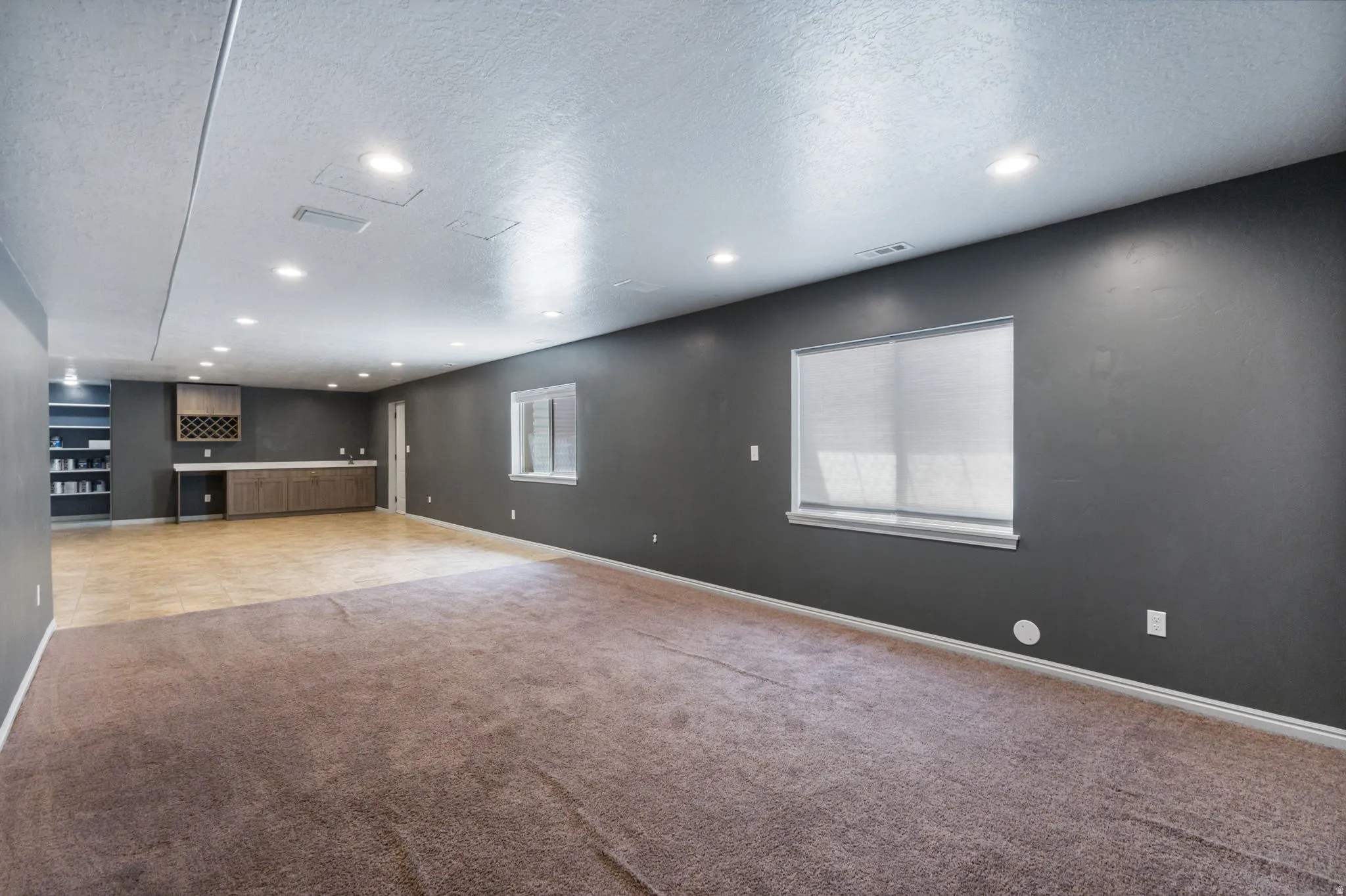 Spacious interior featuring a combination of carpet and hard-surface flooring, multiple recessed lighting fixtures, built-in cabinetry with a wine rack, and a window with blinds