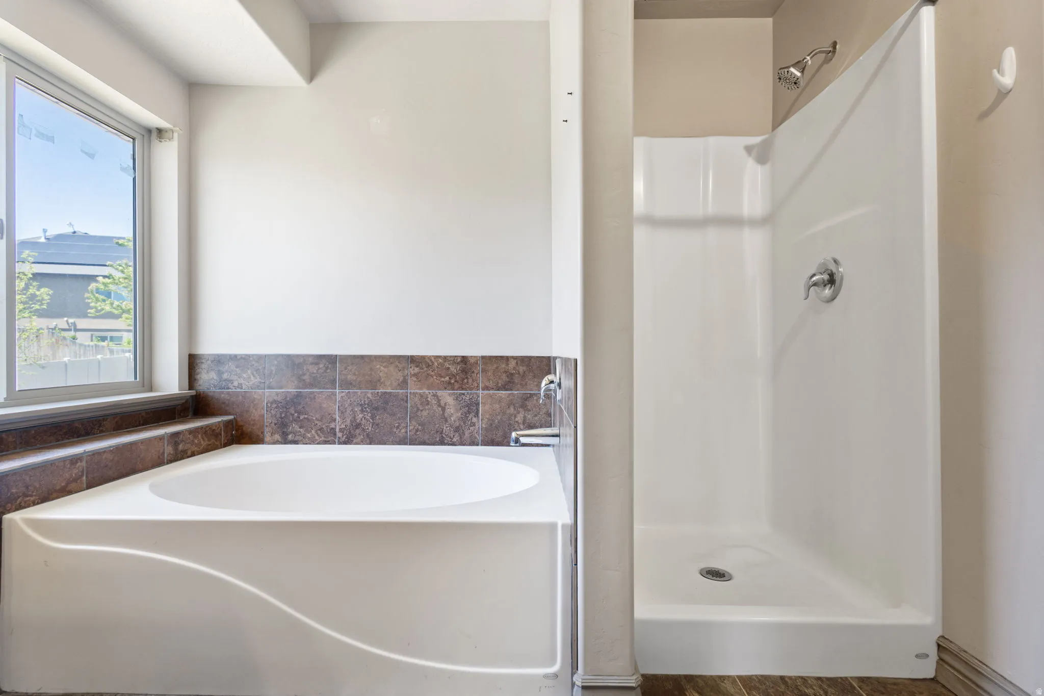 Master Bathroom featuring a white soaking tub with tiled surround, a window, and a stand-up shower with a chrome showerhead