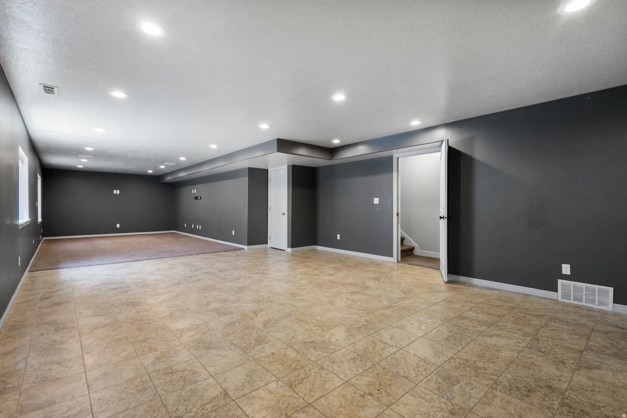 Spacious room featuring neutral tile flooring, recessed lighting, and a distinct carpeted area