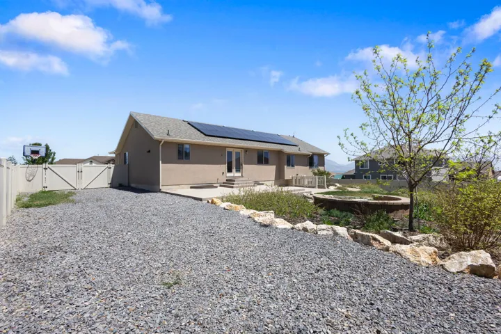 Rear exterior featuring a neutral-toned stucco finish, a composite shingle roof, and integrated solar panels