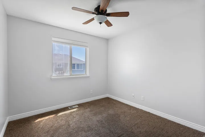 Bright room featuring a ceiling fan with wood-finish blades and integrated lighting, a double-pane window, and neutral-toned carpeting