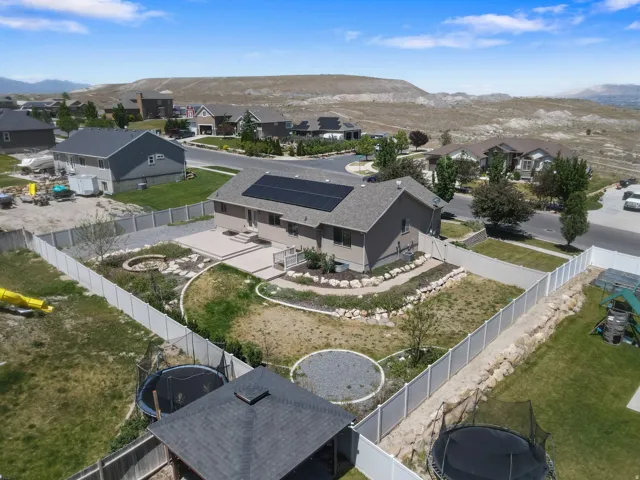Rear exterior featuring an elevated patio, solar panels, and a fenced yard with a fire pit area