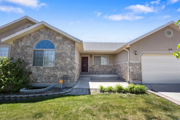 Stone facade home featuring an arched window, a two-car garage, and a paver stone patio