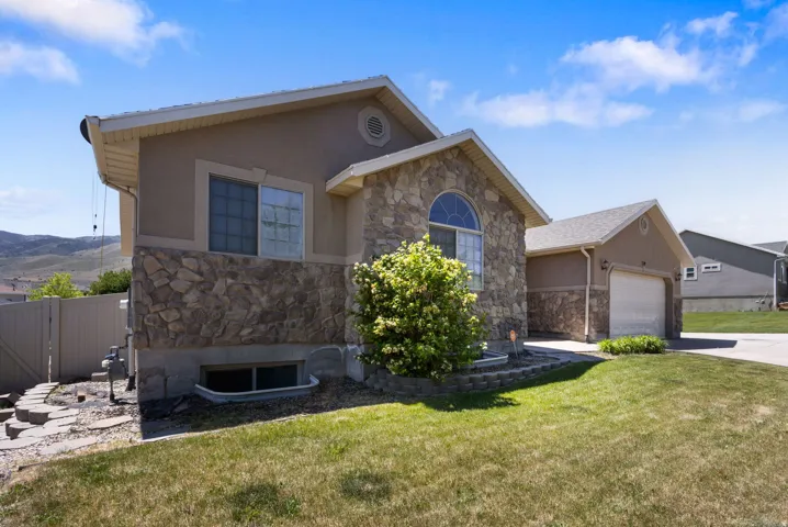 Stone facade home featuring an arched window, a two-car garage, and a manicured front lawn