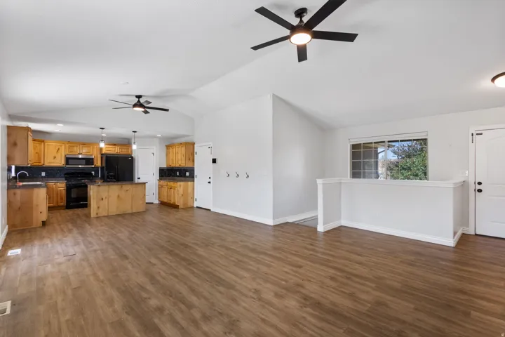 Spacious open-concept interior featuring wood-finish flooring, vaulted ceilings with ceiling fans, and a kitchen with wood cabinetry, black appliances, and pendant lighting