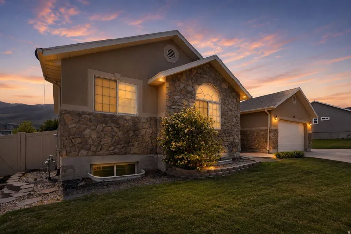 Stone and stucco exterior featuring a two-car garage, arched window, exterior lighting, and a manicured front lawn