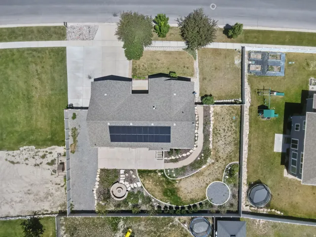 Shingle roof with integrated solar panels, concrete patio, gravel side yard, and landscaped garden beds
