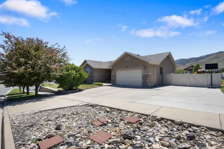 Contemporary stucco and stone-accented residence featuring a two-car garage, expansive concrete driveway, and side yard with a privacy fence