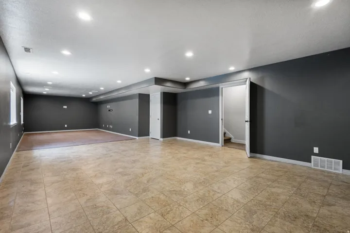 Spacious room featuring neutral tile flooring, recessed lighting, and a distinct carpeted area