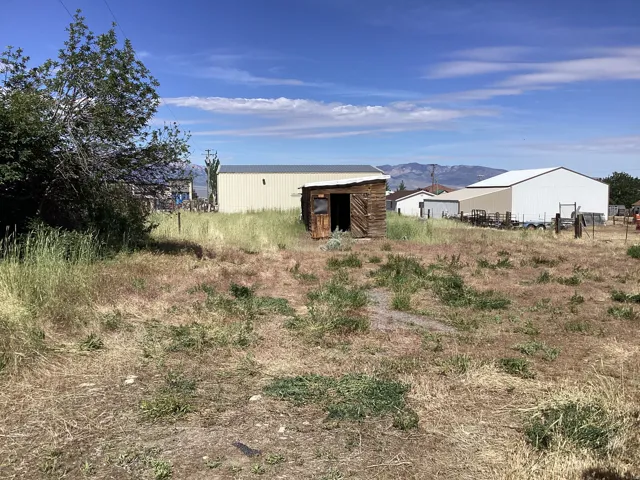 Expansive open lot with a rustic wooden shed, mature trees, and distant mountain ranges
