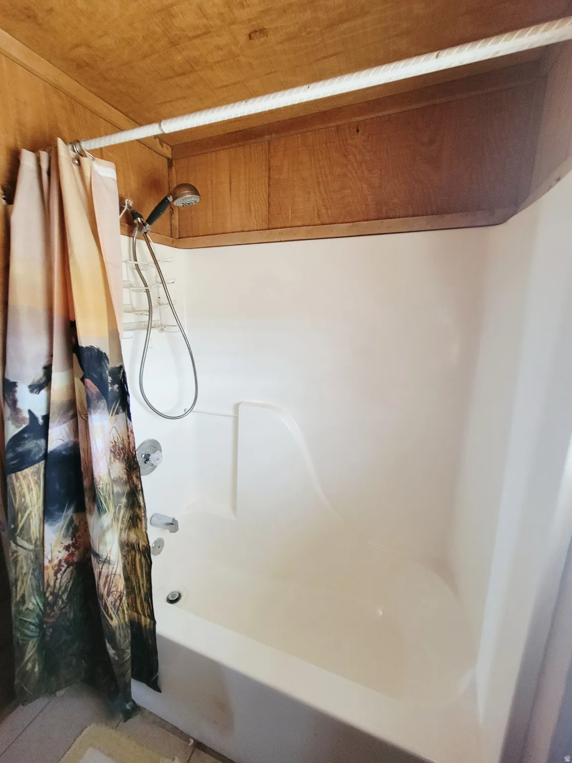 Tub and shower combination featuring a built-in shelf, handheld shower sprayer, and chrome fixtures