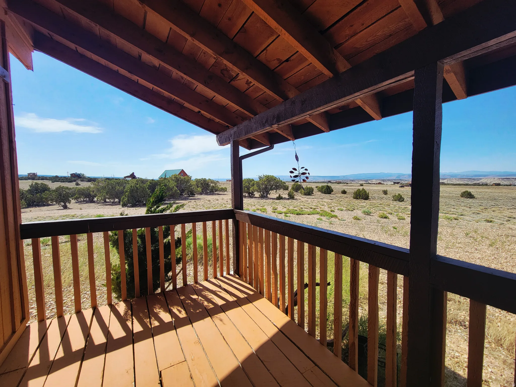Covered wooden porch with exposed rafters, wood flooring, and a wooden railing