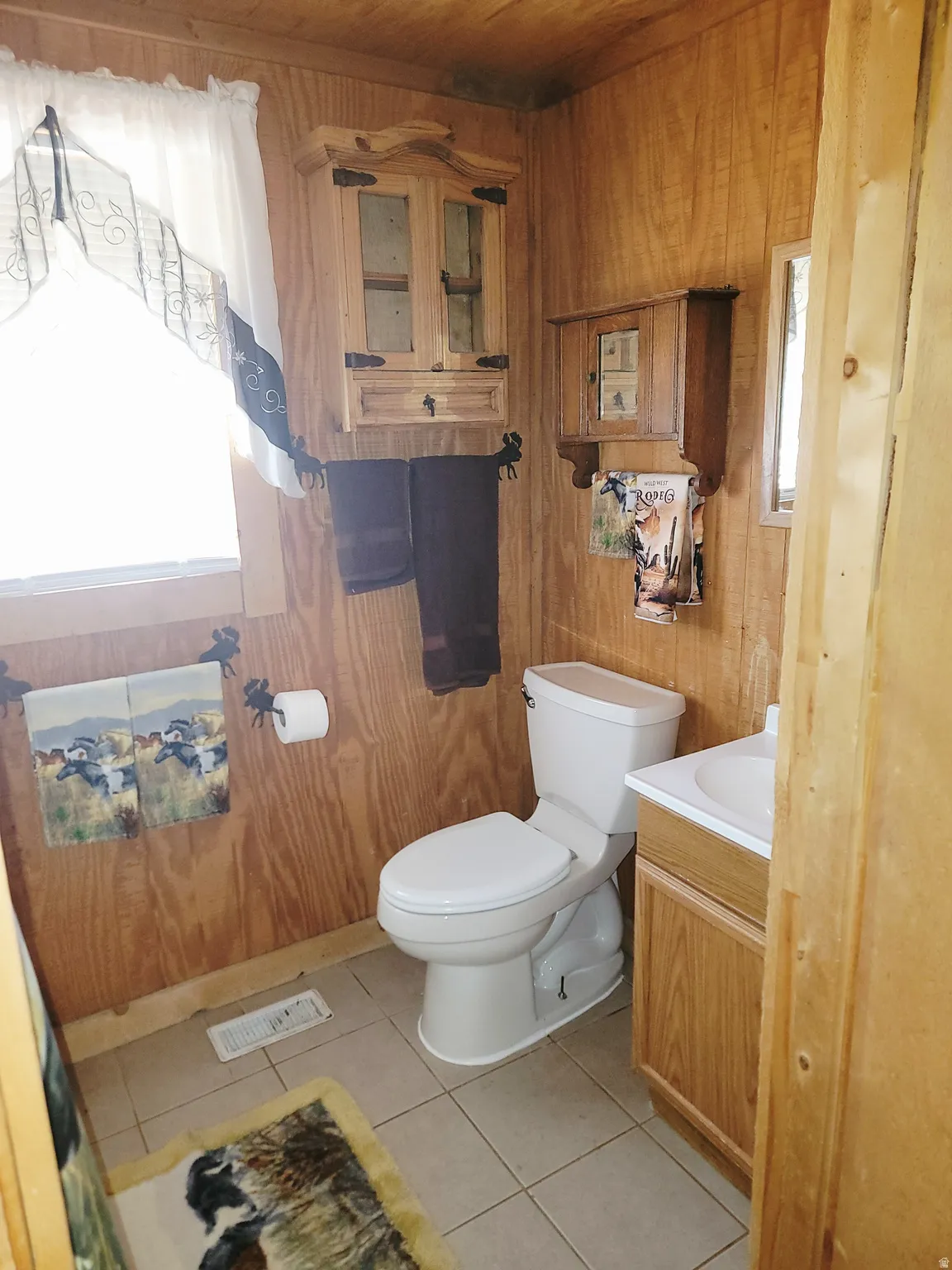 Bathroom featuring wood paneling, a white toilet, a vanity with a built-in sink, and light-colored tile flooring