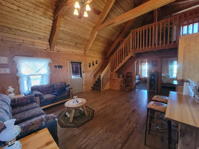 Spacious interior featuring a vaulted ceiling with exposed beams, wood-finish flooring, and a prominent staircase leading to an upper loft area