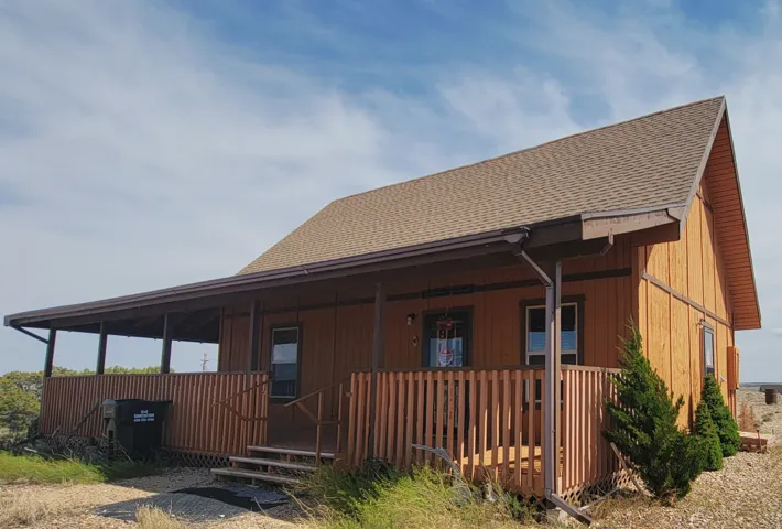 Wood-sided structure featuring a covered front porch with railings, multiple exterior windows, an asphalt shingle roof, and a visible gutter system