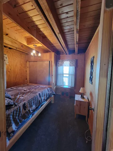 Wood-paneled room featuring exposed wood ceiling joists, dark carpeting, and a window with natural light