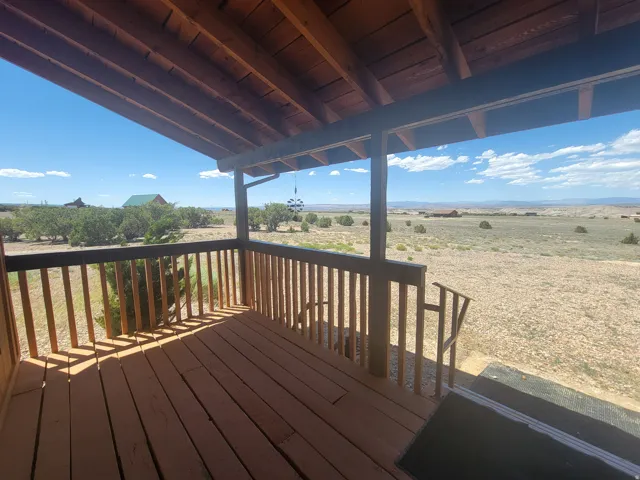 Covered wooden deck featuring a slatted railing system, exposed wood ceiling beams, and expansive desert scenery