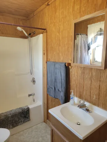 Bathroom featuring a built-in shower/tub combination, wood-panel walls, and a vanity with an integrated sink