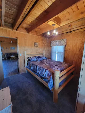 Bedroom featuring wood-finish paneling, exposed wood beam ceiling, and plush carpet flooring